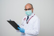 © Chanakon - Asian bald Doctor in white coat, stethoscope, blue glove wearing face mask writing something on clipboard and look into camera isolated on white background.