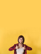© Leila - Portrait beautiful young woman standing in checked shirt and gave thumbs up: vertical banner with space for text, well signed sign and looking at the camera on yellow background