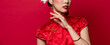 Asian woman in traditonal Chinese Cheongsam dress touching her face in isolated red banner background
