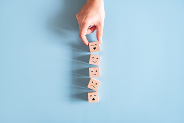 Customer service evaluation and satisfaction survey concepts. The client's hand picked the happy face smile face icon symbol on wooden cube on blue paper background.