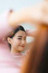 Beautiful asian woman tying hair looking at mirror.