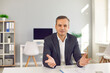 © Studio Romantic - Portrait of happy businessman sitting at desk in office, looking at camera and talking