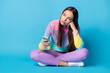 © deagreez - Portrait of pretty sad lonely girl sitting lotus position crossed legs using gadget waiting response isolated bright blue color background