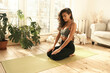 Indoor image of calm beautiful young Latin woman with tanned fit body practicing meditation, sitting on floor, doing Vajrasana pose, keeping eyes closed, taking deep breaths. Recreation and harmony
