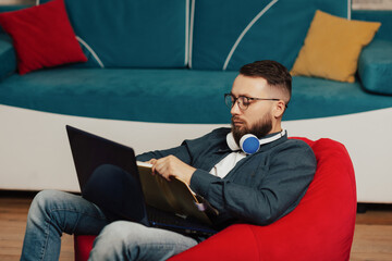 Businessman with headphones  is writing into his notepad while sitting on armchair at home.