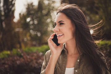 Sticker - Photo of lovely dreamy young woman look side hold telephone speak toothy smile wear brown shirt park street outside