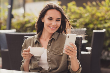 Sticker - Photo portrait of beautiful girl holding cup of coffee and phone in hands sitting in cafe browsing social networks