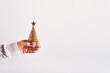 Female hand in white sweater holding golden Christmas tree with star on white background, copy space