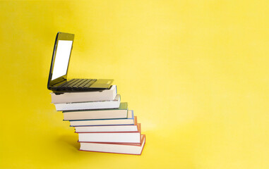 laptop and stack of books on yellow background