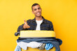 Traveler man with a suitcase full of clothes over isolated yellow background handshaking after good deal