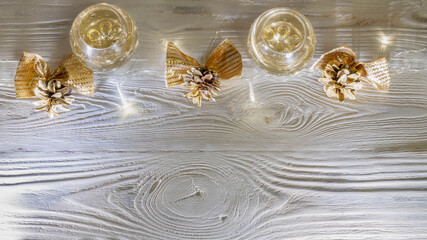 Christmas background with glasses of champagne, golden pine cones and glowing garland of light bulbs on a white wooden background.