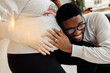 © shunevich - Close up of charming African American man hug pregnant belly of lovely wife, smiling, happy couple expect for a baby, excited about parenting, motherhood and fatherhood concept
