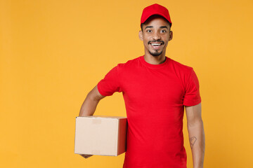 Wall Mural - Delivery employee african man 20s in red cap blank print t-shirt uniform work courier service on quarantine coronavirus covid-19 virus concept hold cardboard box isolated on yellow background studio.