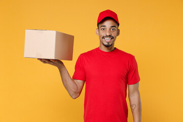 Wall Mural - Delivery employee african man 20s in red cap blank print t-shirt uniform work courier service on quarantine coronavirus covid-19 virus concept hold cardboard box isolated on yellow background studio.