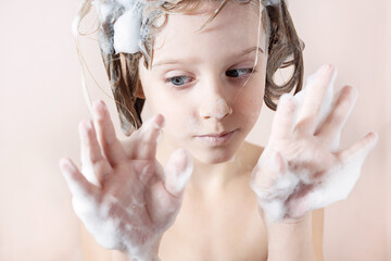 Wall Mural - adorable little girl with blue eyes washes her hair in the bathroom and laughs, foam on her head
