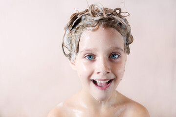 Wall Mural - a little blonde girl with a soapy head smiles in the bathroom on a pink background