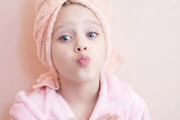 Wall Mural - a little girl with blue eyes in a pink robe and a pink towel on her head after a bath smiles and loo
