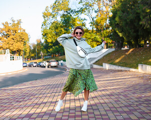 Wall Mural - Smiling blonde woman with short hair laughing on the street cheerfully. Lovely young lady feeling happy in the autumn park, moves outside and smiles. Happy girl with handbag walks.