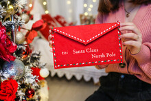 Hand Holds An Envelope With A Letter To Santa Claus On The Background Of A Christmas Tree