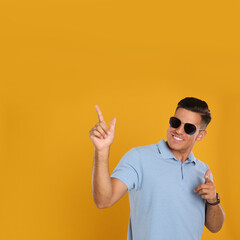 Wall Mural - Handsome man wearing sunglasses on yellow background