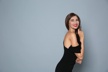 Happy woman in black dress on grey background, space for text. Christmas party