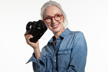 Smiling Stylish Energetic Mature Female Photographer In Glasses Posing With Digital Camera On White Background. Portrait Of Positive Gray Haired Middle Aged Lady. Free Time, Age And Hobby Concept.
