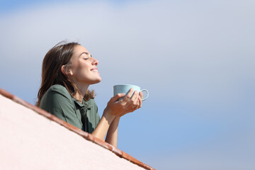 Wall Mural - Happy woman drinking coffee breathing fresh air from balcony