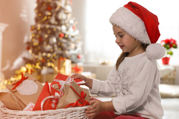 Canvas Print - Cute little girl in Santa hat taking gift from Christmas advent calendar at home