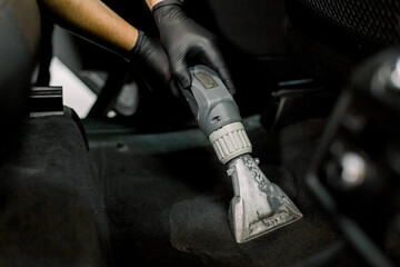 Cropped close up shot of hands of African male worker at auto service station, using vacuum cleaner in car, remowing the dust and sand. Vacuum cleaning inside the car