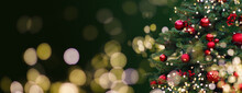 Closeup Of Festively Decorated Outdoor Christmas Tree With Bright Red Balls On Blurred Sparkling Fairy Background. Defocused Garland Lights, Bokeh Effect