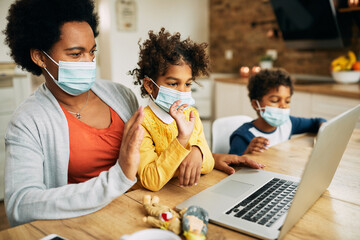 Wall Mural - Black mother and kids with face masks having video call over laptop at home.