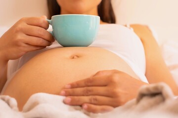 Pregnant woman drinking a cup of coffee and relaxing at home.