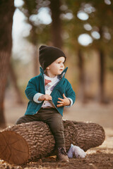 Wall Mural - a boy in a green warm jacket and a knitted hat is sitting on a tree. He's happy.