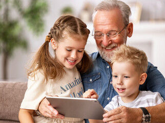 Wall Mural - Grandfather and grandchildren using tablet on sofa.