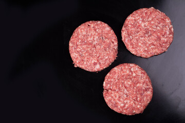 raw burgers on black background