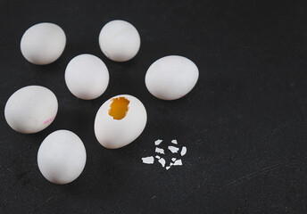 White eggs on black.
Seven white eggs and one broken egg on the left against a black background with space for text on the right, side view close-up.