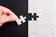 © sorapop - Top view flat lay of hand-holding last piece white paper jigsaw puzzle game last pieces put to place for solve problem complete mission, studio shot on a black background, quiz calculation concept