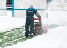 Man Using A Snow Blower To Remove Large Amounts Of Snow On Football Field. Man Cleans Snow With A Snow-removing Machine On Soccer Pitch.