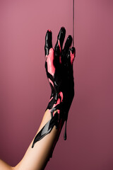 Wall Mural - partial view of hand with dripping black paint isolated on pink, stock image