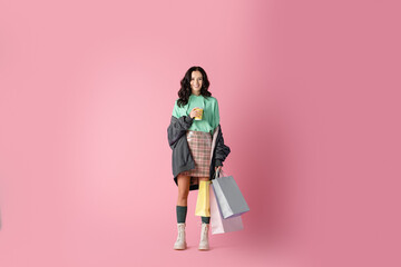 Wall Mural -  brunette young woman in casual winter outfit with shopping bags and coffee to go on pink background