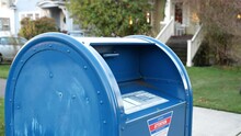 Woman Drops A Letter Into A Blue USPS Mail Box