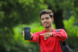 © PRASANNAPIX - Young indian college student showing smart phone over nature background