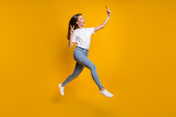 Full length body size photo of female influencer taking selfie showing v-sign isolated on vibrant yellow color background