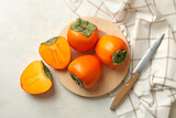 Plate with persimmon, knife and kitchen towel on white table