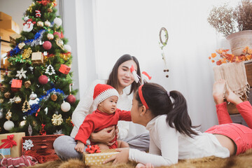 Canvas Print - parent and two little children having fun and playing together near christmas tree indoors. merry christmas and happy holidays. cheerful mom and her cute daughters girls exchanging gifts.