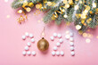 Figures 2021 made from snowballs and a Christmas ball on pink background, spruce branches and golden bokeh lights