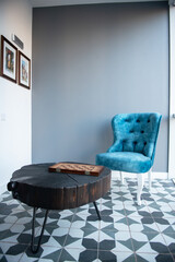 Modern design home interior with elegant blue chair in retro style and black wooden coffee table over gray wall. Stylish home decor