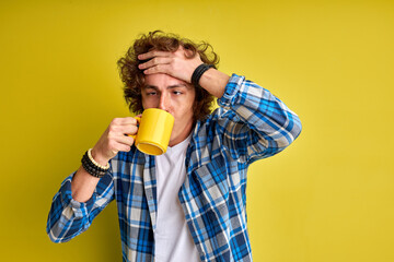 handsome caucasian student boy begins morning from cup of hot tea, stand posing isolated over green background