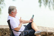 © sutthichai - Asian senior male using mobile phone for video call communication with his family while vacation next to the beach.