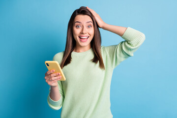 Wall Mural - Photo portrait of happy woman touching head with one hand holding phone isolated on pastel blue colored background